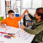 A boy with down syndrome is high five in a classroom with his teacher